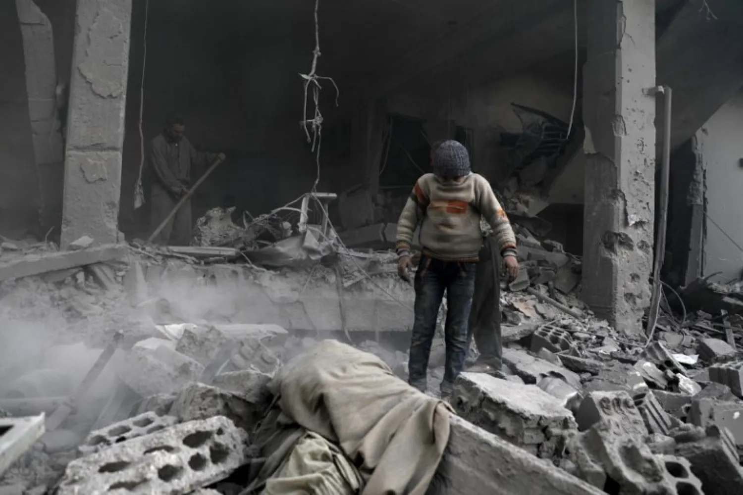 A Syrian boy covers his face as he stands amid destroyed buildings following regime air strikes in the Eastern Ghouta rebel-held enclave of Douma, on the outskirts of the capital Damascus on March 19, 2018. HAMZA AL-AJWEH / AFP