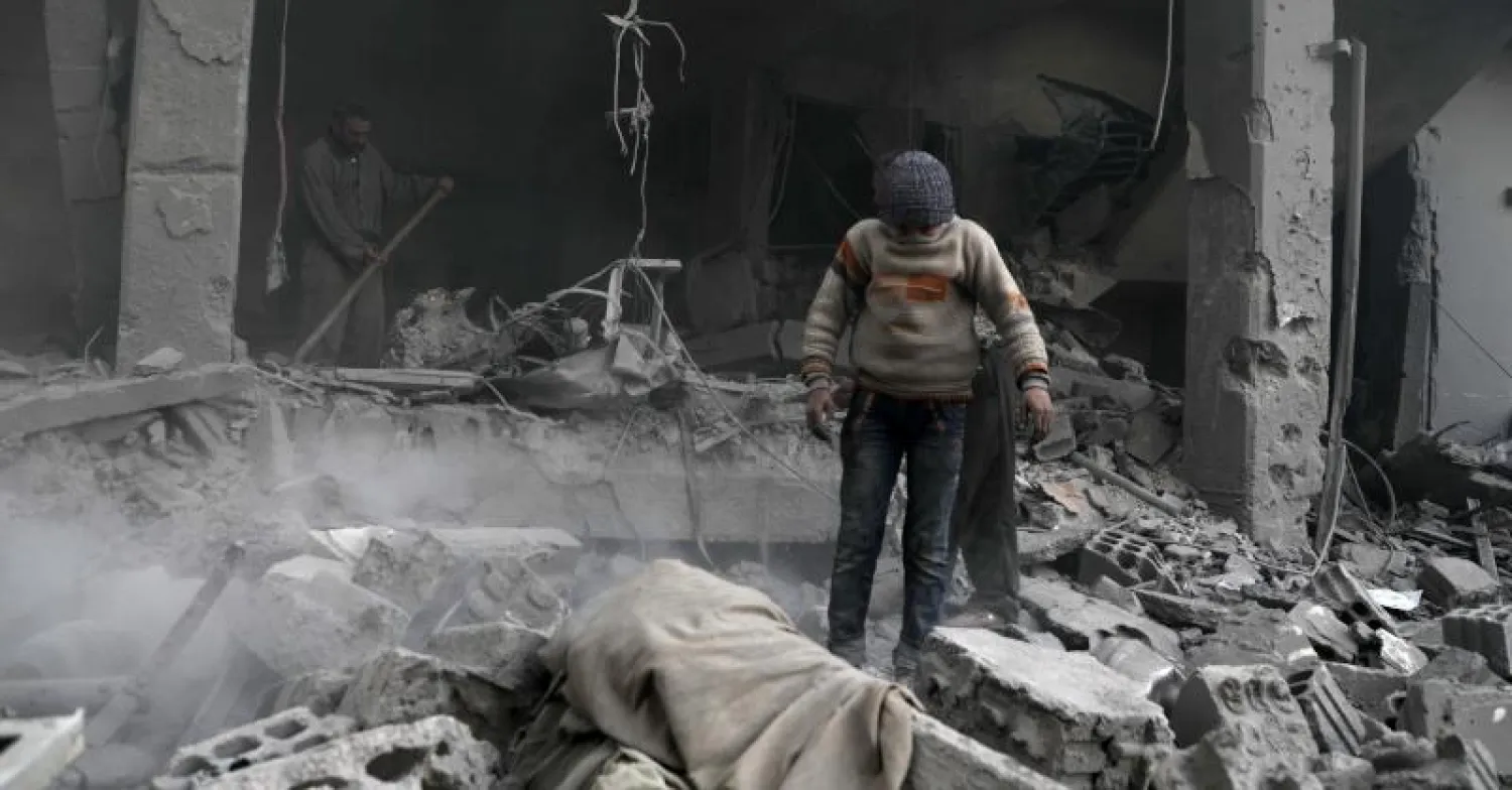 طفل سوري يغطي وجهه وهو يقف وسط أبنية مدمرة في أعقاب غارات جوية للنظام على جيب دوما شرق الغوطة (أ.ف.ب)