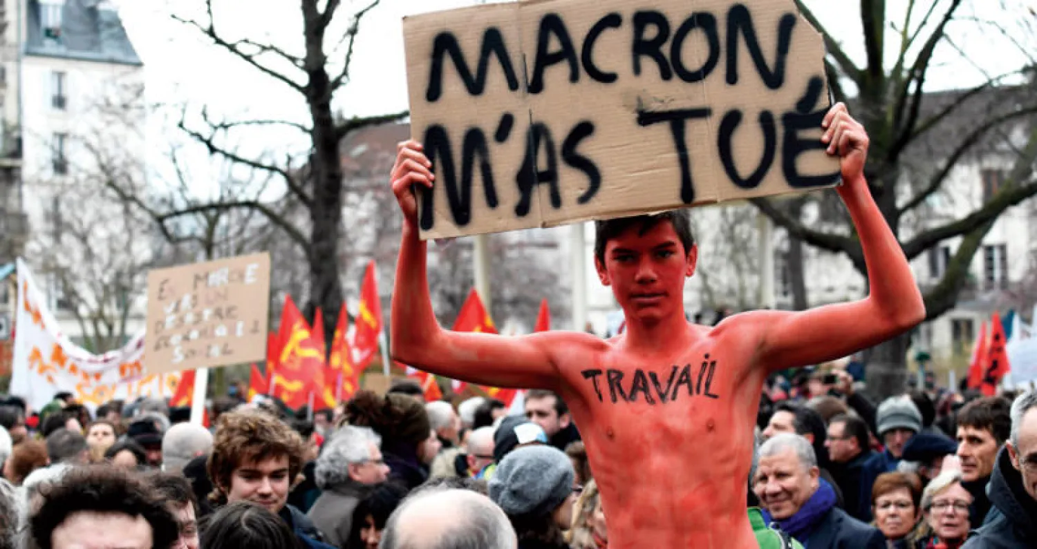 شاب فرنسي كتب على صدره عبارة «عمل» ويحمل لافتة تقول «ماكرون قتلني» خلال مظاهرة مناهضة لإصلاحات الحكومة في باريس في الآونة الأخيرة (ا.ف.ب)