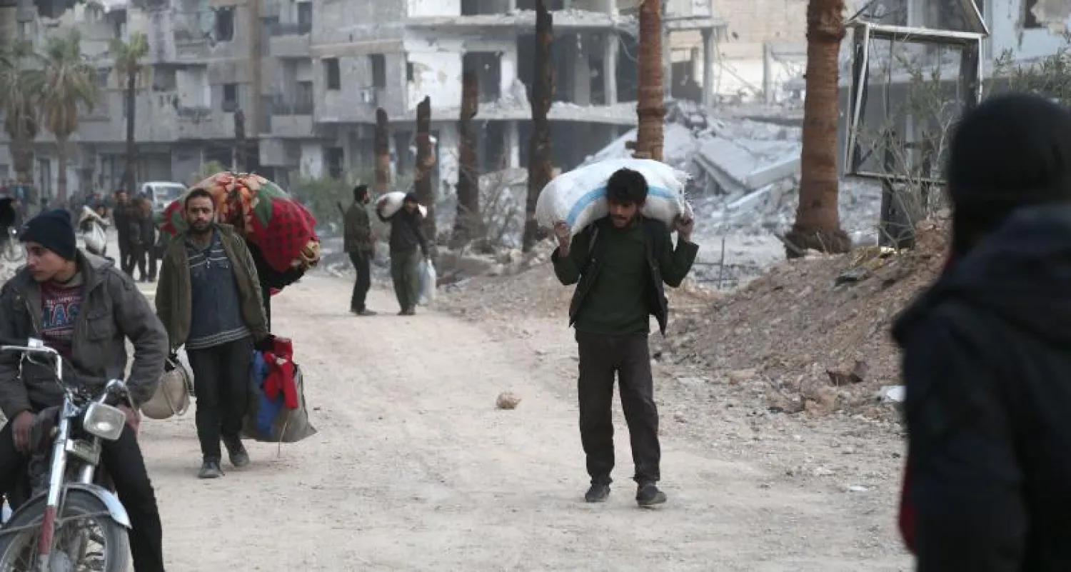 سوريون يحملون متعلقاتهم بينما يسيرون في شارع مدمر استعداداً لإخلاء أحد الجيوب القليلة المتبقية التي تسيطر عليها المعارضة في عربين بالغوطة الشرقية (أ.ف.ب)