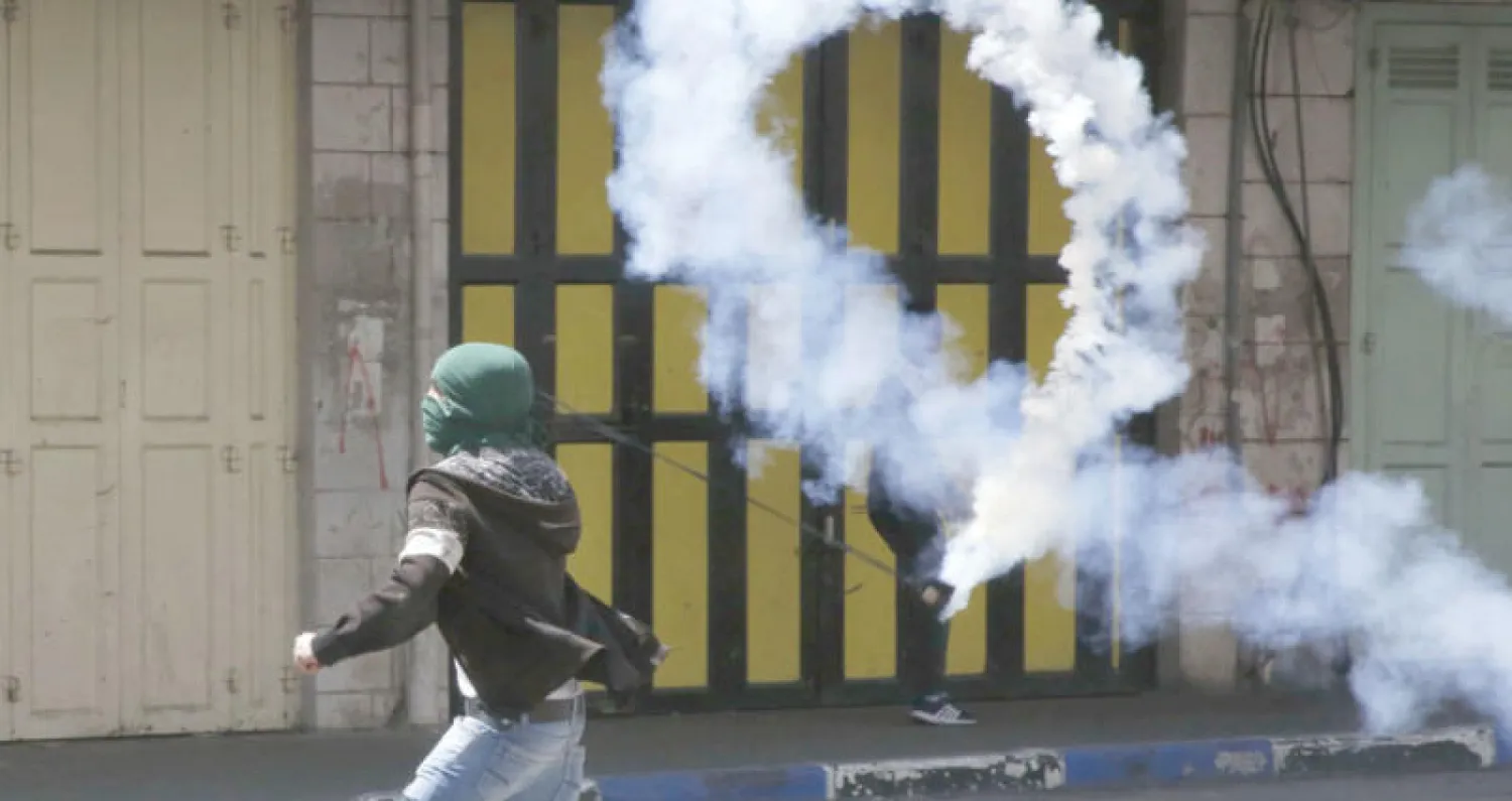 فلسطيني يعيد رمي عبوة مسيلة للدموع في اتجاه الجنود الإسرائيليين في مدينة الخليل أمس (أ.ف.ب)