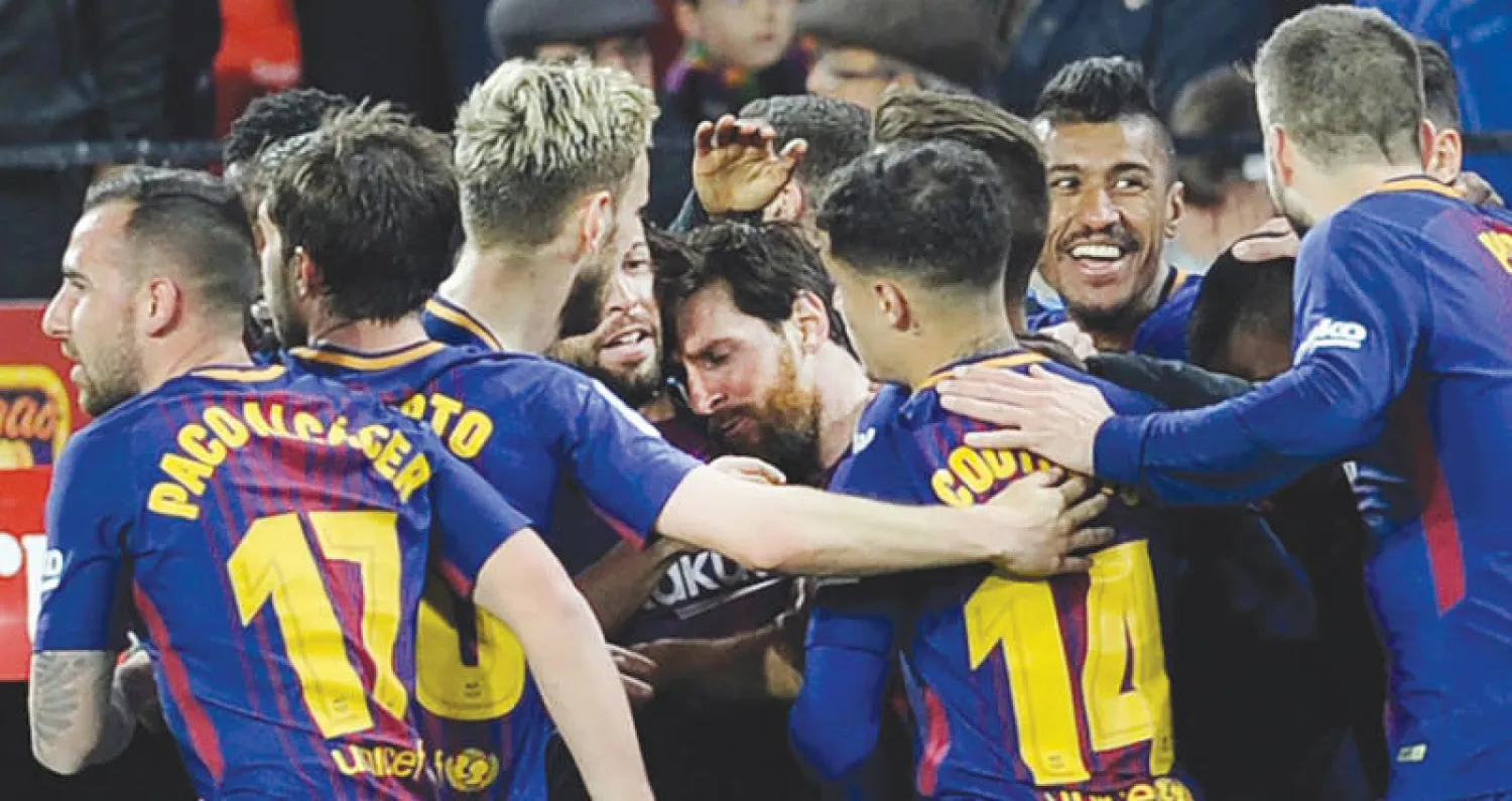 لاعبو برشلونة يحيطون بميسي بعد تسجيله هدف الإنقاذ أمام إشبيلية (أ.ف.ب)