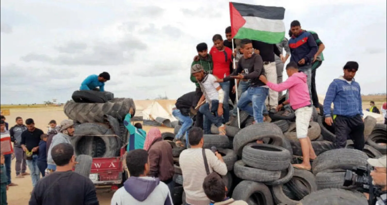 شبان يرفعون العلم الفلسطيني على كومة من إطارات السيارات
