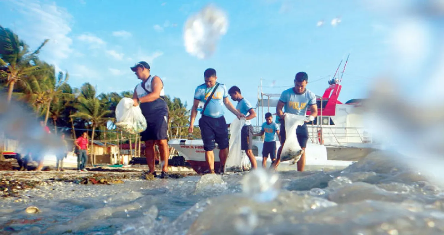 رجال الشرطة الفلبينية يجمعون الحشائش البحرية من أحد شواطئ بوراكاي (إ.ب.أ)