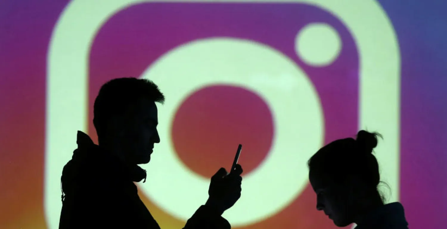 مستخدمان يقفان أمام شعار تطبيق «إنستغرام» (رويترز)
