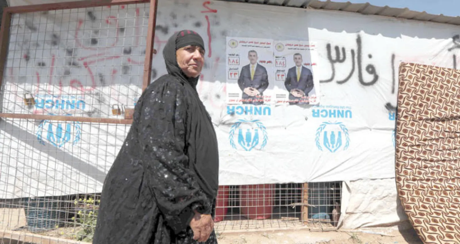 نازحة من الموصل تمر أمام ملصق انتخابي في مخيم حسن شام للنازحين أمس (أ.ف.ب)