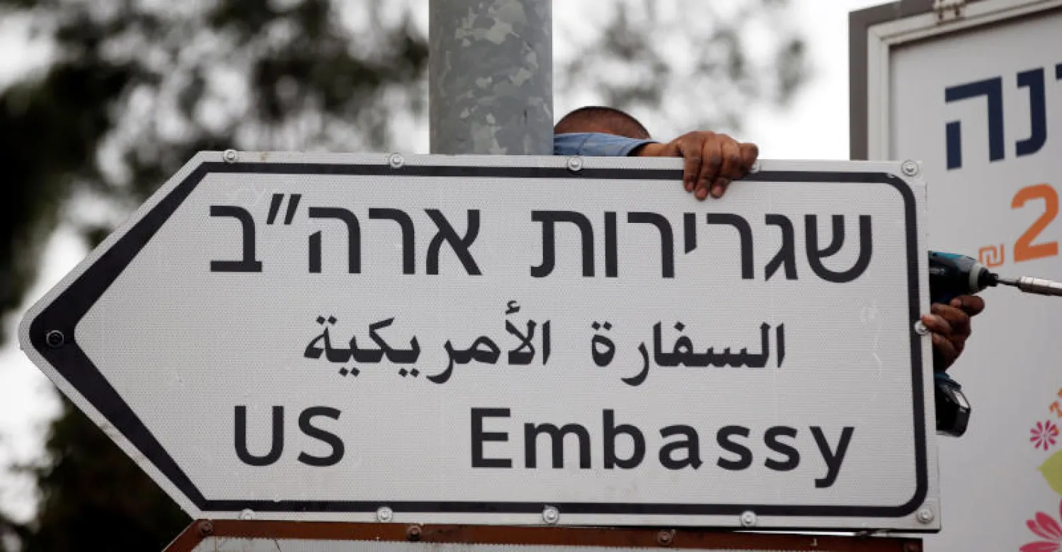 عامل يعلق لافتة طريق في القدس مكتوبا عليها «السفارة الأميركية» (رويترز) 