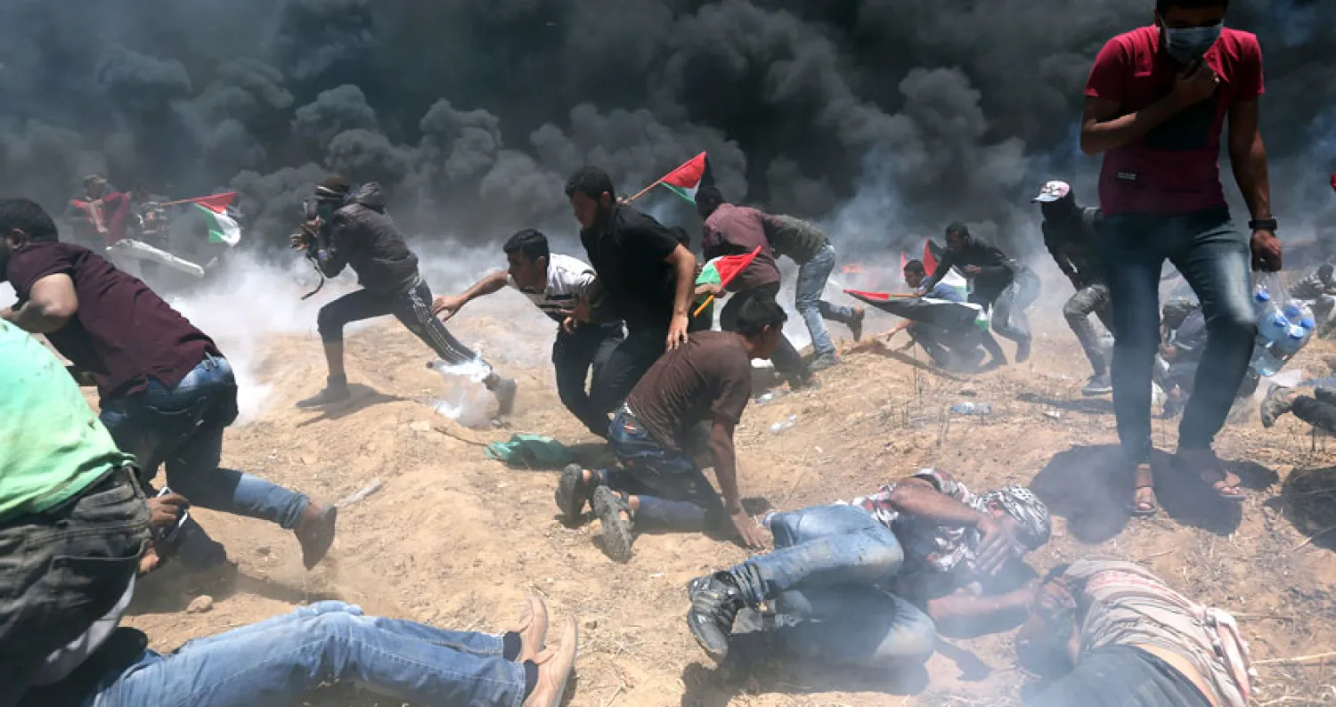 متظاهرون فلسطينيون ينظرون إلى الغاز المسيل للدموع والدخان المتصاعد من الإطارات المحترقة شرق مدينة غزة (أ.ف.ب)