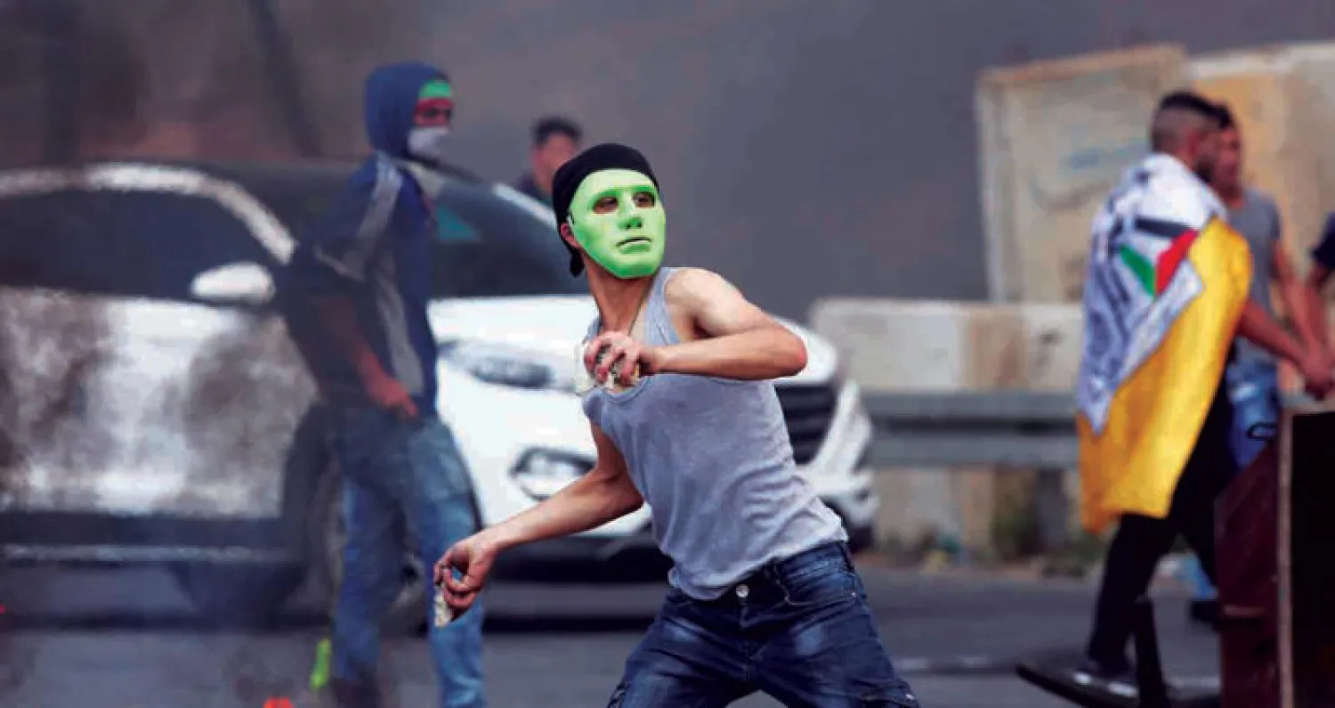 فلسطيني يرمي القوات الإسرائيلية بالحجارة في مظاهرة احتجاجية بالضفة الغربية على نقل السفارة الأميركية إلى القدس (إ.ب.أ)