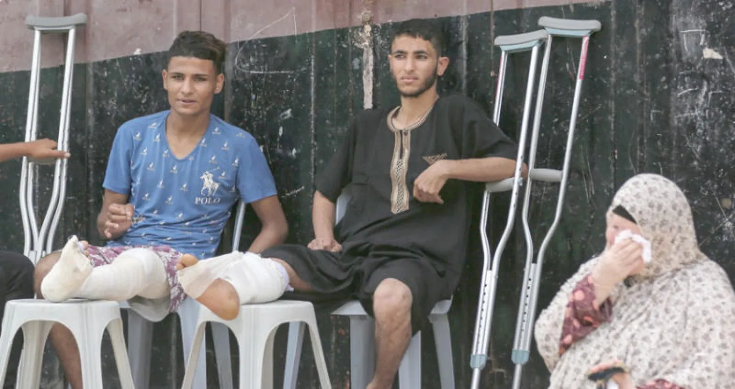 فلسطينيان مصابان يحضران جنازة معين الساعي الذي توفي متأثراً بجروحه في مدينة غزة أمس (أ.ف.ب)