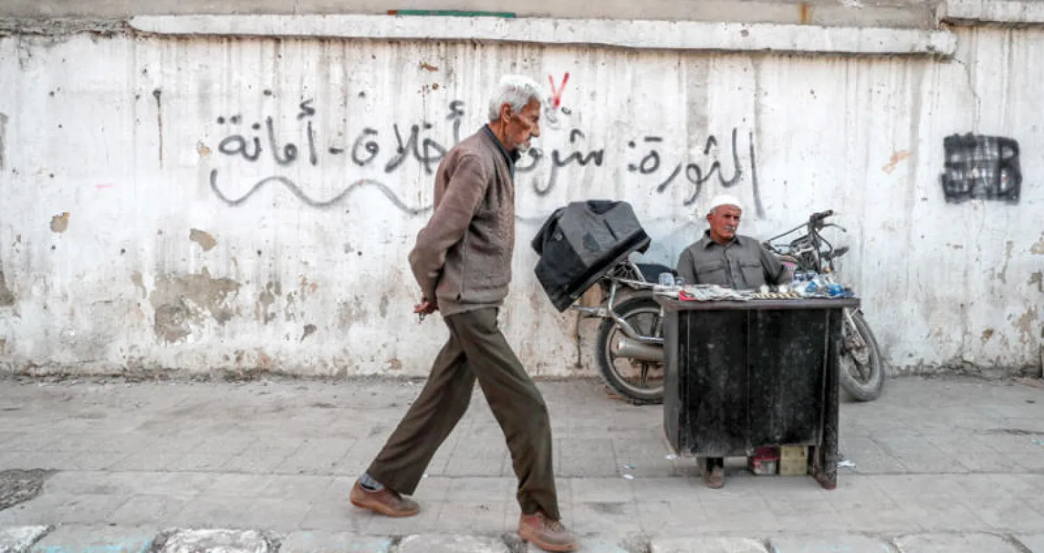 رجل يسير واخر يجلس في شارع في عفرين شمال سوريا أمس (إ.ب.أ)