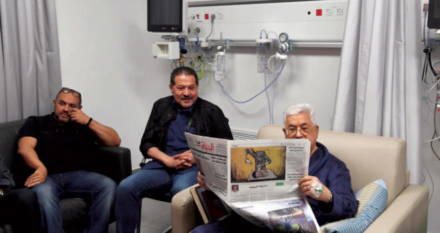 عباس في المستشفى يقرأ صحيفة محلية وإلى جانبه ولداه (إ.ب.أ)