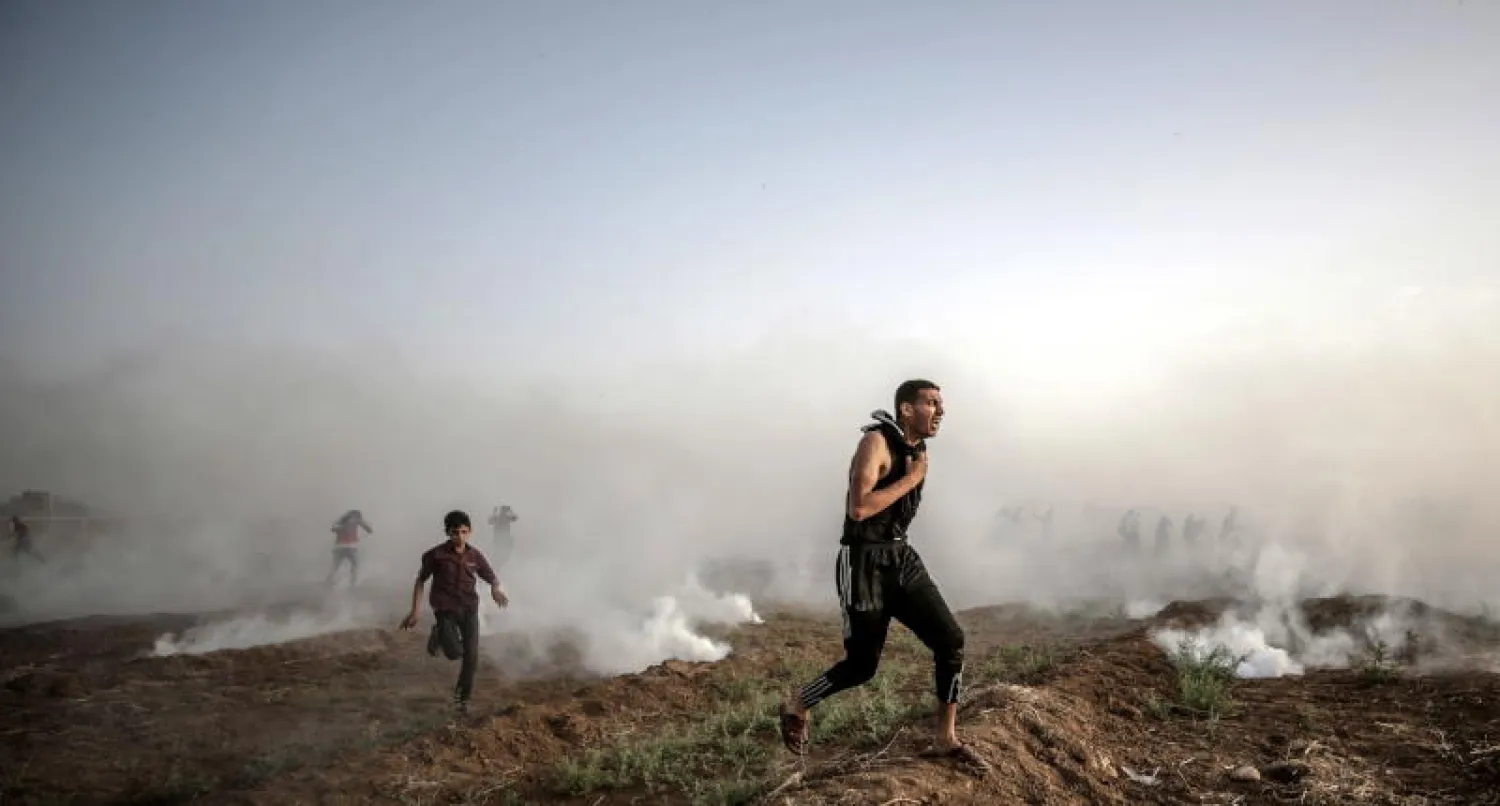 متظاهرون فلسطينيون يهربون من الغاز المسيل للدموع الإسرائيلي أثناء الاشتباكات القريبة من الحدود بين إسرائيل وقطاع غزة (أ.ف.ب)