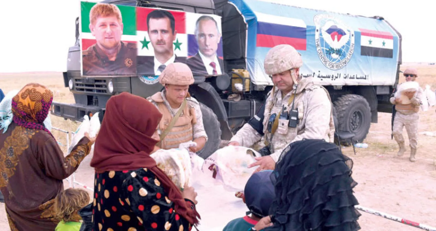 الشرطة الروسية توزع مساعدات على مدنيين في نقطة تفتيش أبو الضهور في ريف إدلب الشرقي أمس وبدت شاحنة تحمل صور الرؤساء الروسي فلاديمير بوتين والسوري بشار الأسد والشيشاني رمضان قاديروف  (أ.ف.ب)