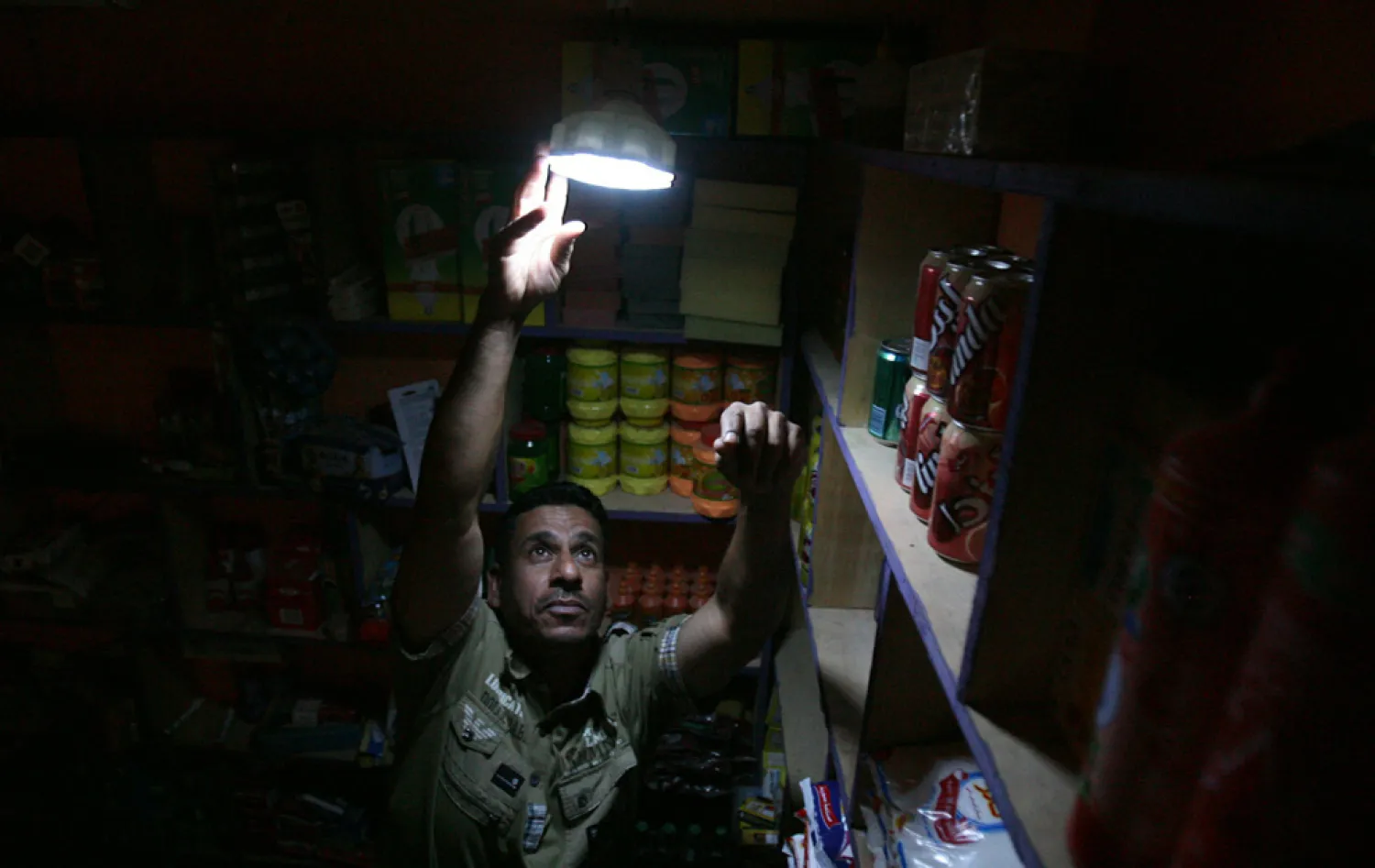 An Iraqi grocer fixes a lamp with a rechargeable battery in his shop during power outage in Baghdad. (AFP)