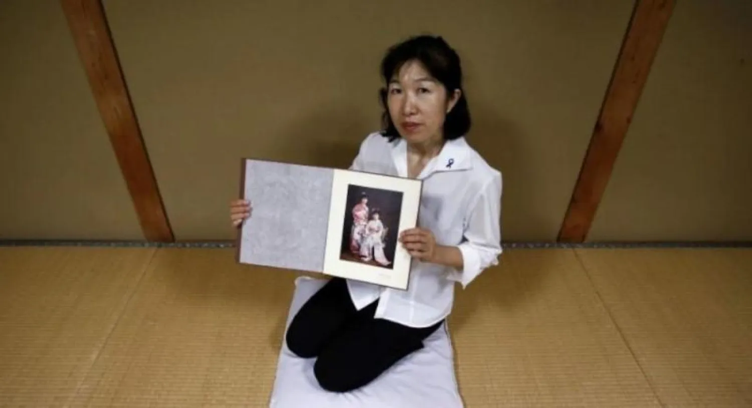 المعلمة اليابانية ميسا موريموتو تعرض صورة قديمة لها مع شقيقتها التوأم ميهو التقطت لهما عام 1984 (رويترز)