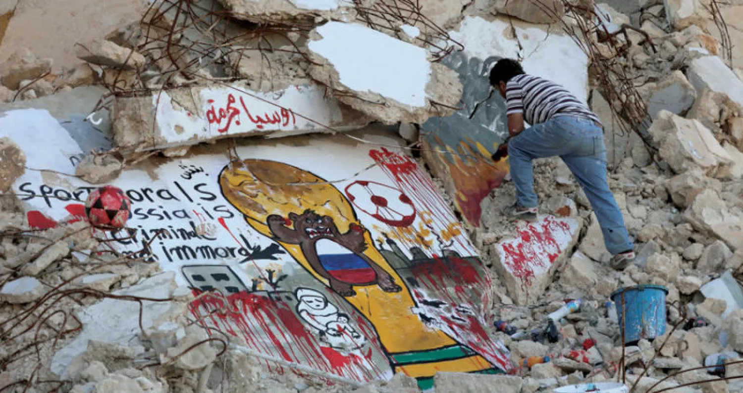 فنان غرافيتي ينجز جدارية فوق مبنى هدمته غارات الطيران الحربي للنظام المدعوم من روسيا في بلدة بنش بمحافطة إدلب (أ.ف.ب)