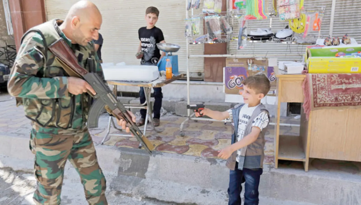 جندي سوري يداعب طفلاً يحمل مسدساً بلاستيكياً في دوما بالغوطة الشرقية أمس (إ.ب.أ)