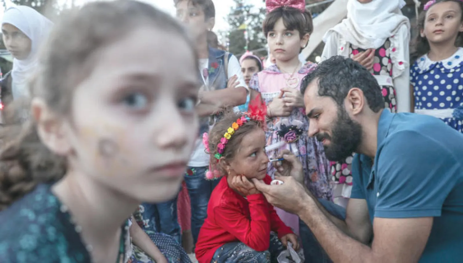 أحد المتطوعين يزين وجوه أطفال بالرسوم في إدلب بمناسبة احتفالهم بعيد الفطر (إ.ب.أ)