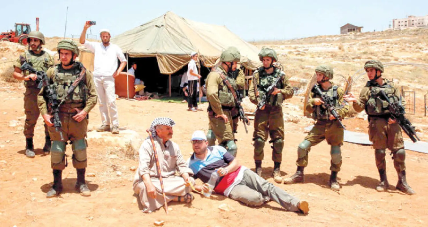 فلسطينيون وسط جنود إسرائيليين خلال احتجاجهم أمام خيمة نصبها مستوطنون على أرض مهددة بالمصادرة شرق مدينة الخليل أمس (أ.ف.ب)