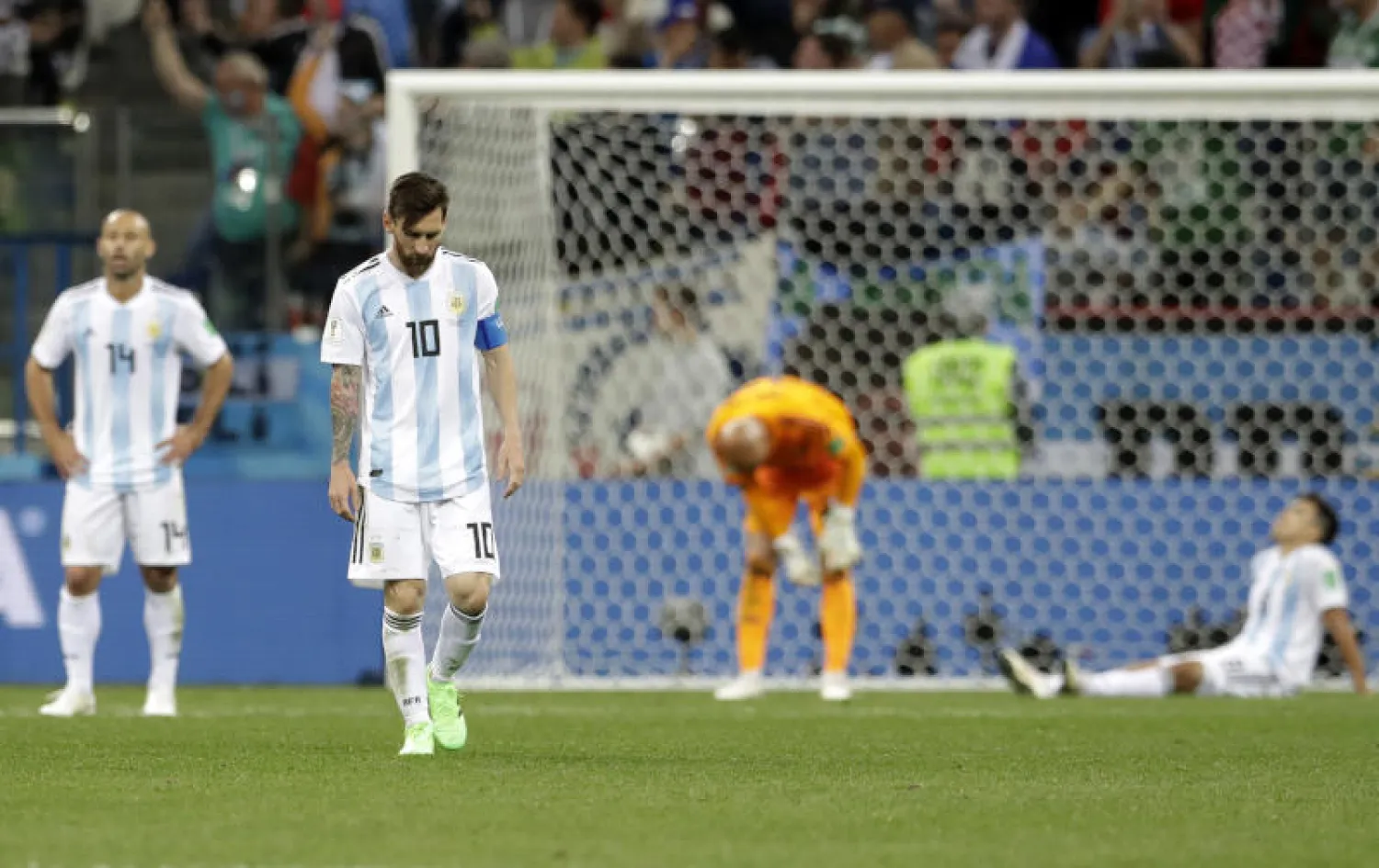ميسي يسير حزينا بعد تلقي خسارة فريقه الكبيرة أمام كرواتيا فيما ارتمى زملاؤه على الأرض (أسوشيتد برس)