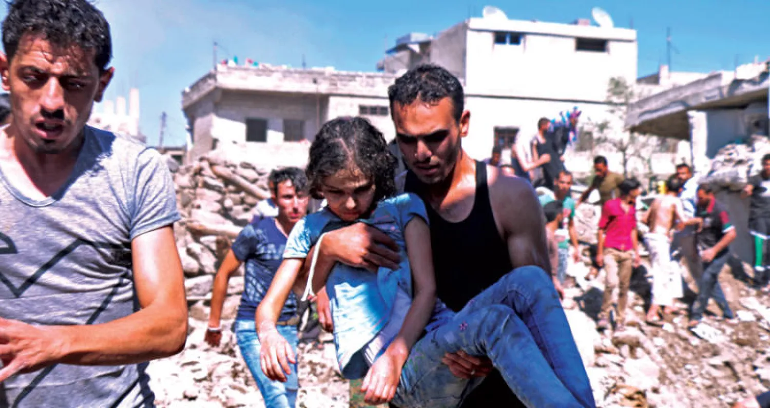 سوري يجلي طفلة مصابة من منطقة بمدينة درعا استهدفتها غارات لطائرات النظام وروسيا أمس (أ.ف.ب)