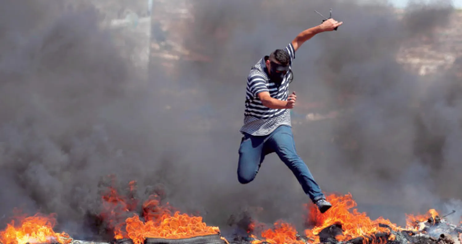فلسطيني يقفز فوق إطارات مشتعلة خلال احتجاجات قرب مستوطنة بيت إيل المجاورة لرام الله بالضفة الغربية أمس (أ.ف.ب)