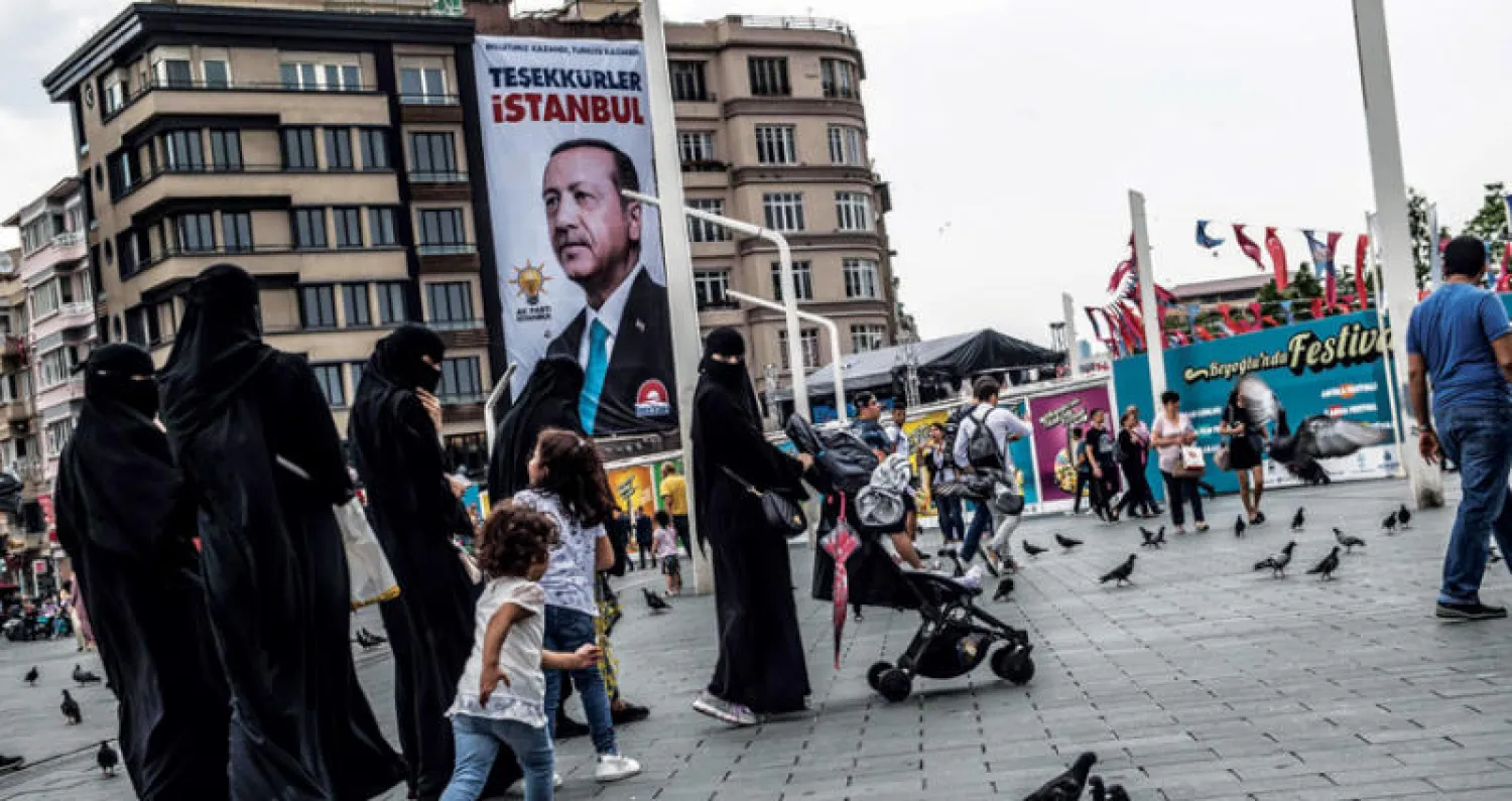 مارة يتنزهون قرب لافتة عليها صورة إردوغان وشعار «شكرا إسطنبول» بعد الانتخابات التشريعية الخميس الماضي (أ.ف.ب)