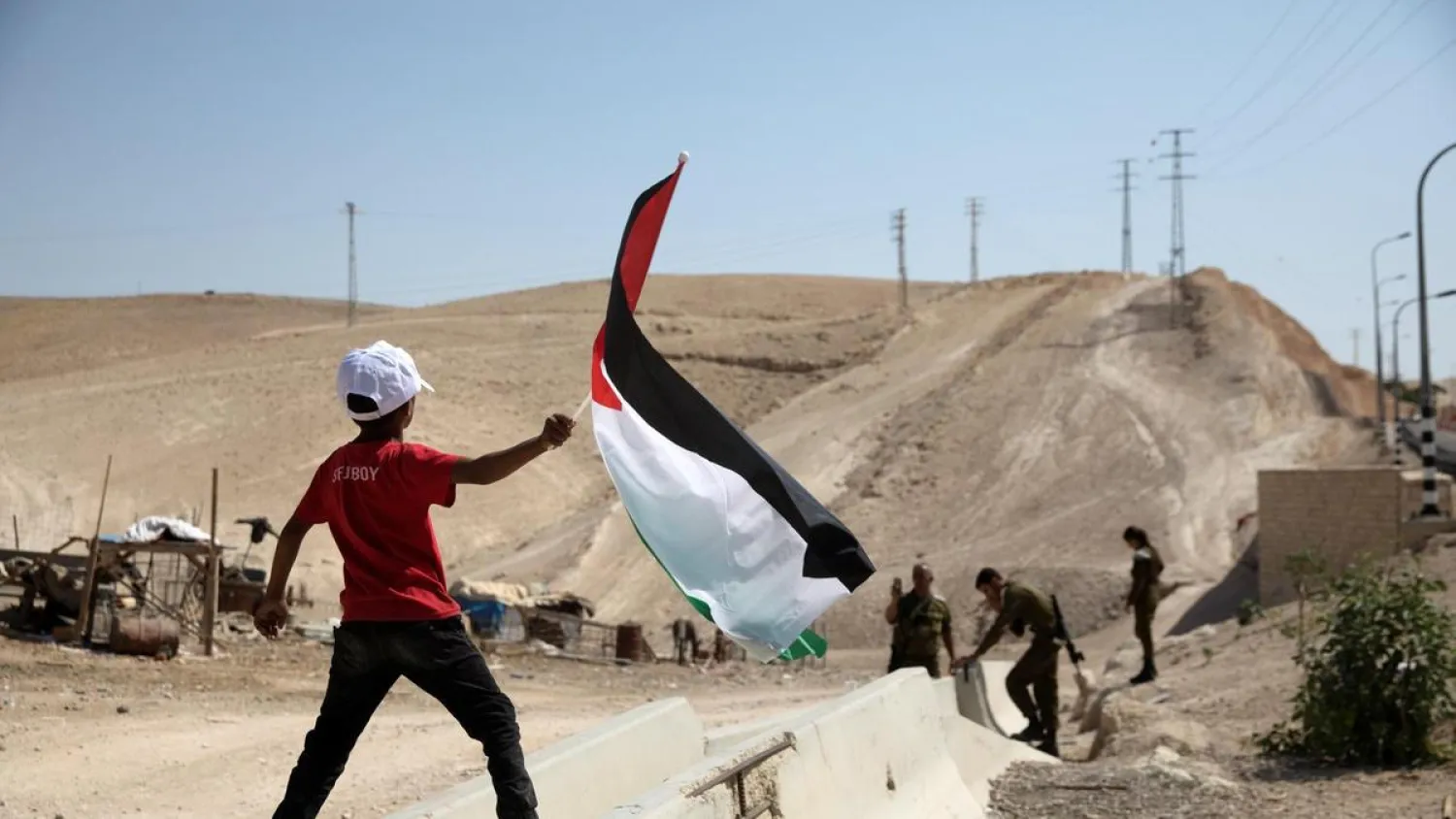 A Bedouin boy waves a Palestinian flag in front of Israeli soldiers at Khan Al-Ahmar. (Reuters)