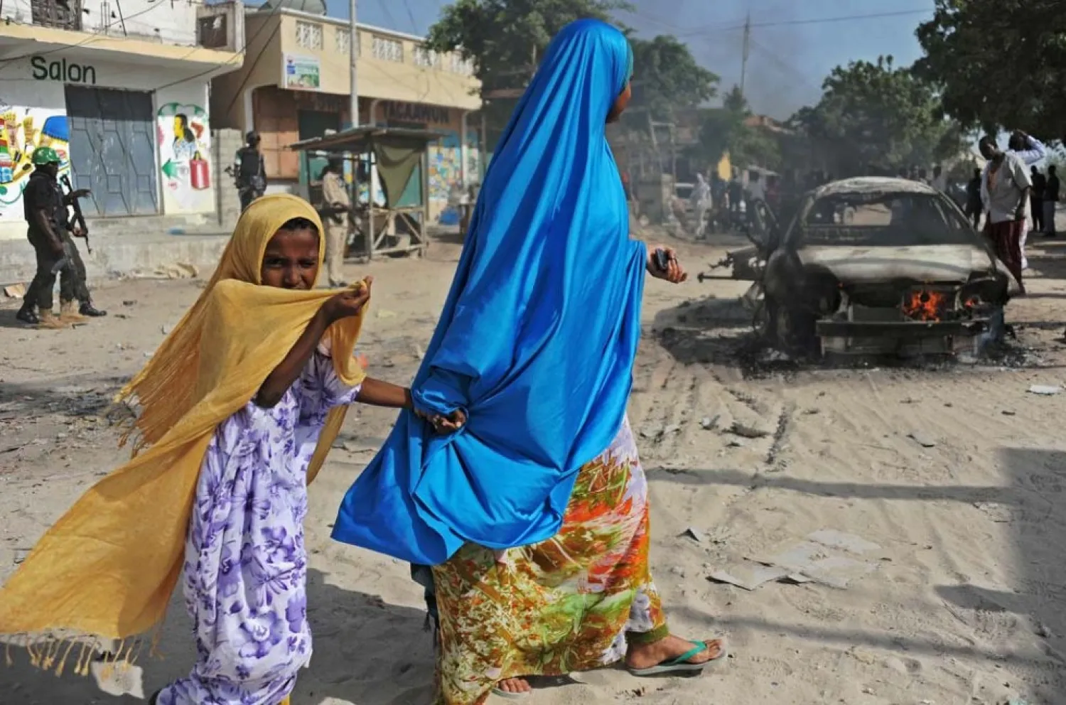 A mother and a child walk past the wreckage of a car bomb in the Wardhigley District, south of Mogadishu, on February 27, 2015 (AFP Photo / Mohamed Abdiwahab)
