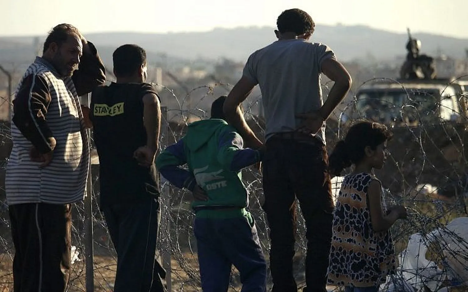 A member of the Jordanian army stands on a jeep behind barbed wire as displaced Syrians from Daraa province fleeing shelling by pro-government forces are seen in a makeshift camp, near the town of Naseeb, southern Syria, on July 2, 2018. (AFP Photo/Mohamad Abazeed)