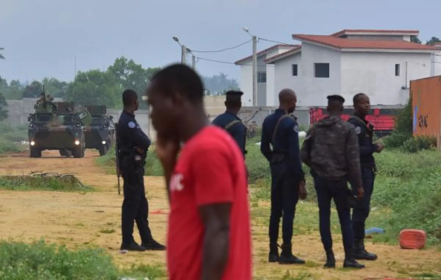 A man walks by Ivory Coast gendarmes and soldiers on July 11, 2018, following the crash of a French army Gazelle helicopter near a residential area near Abidjan, on July 10, 2018.  AFP PHOTO / ISSOUF SANOGO
