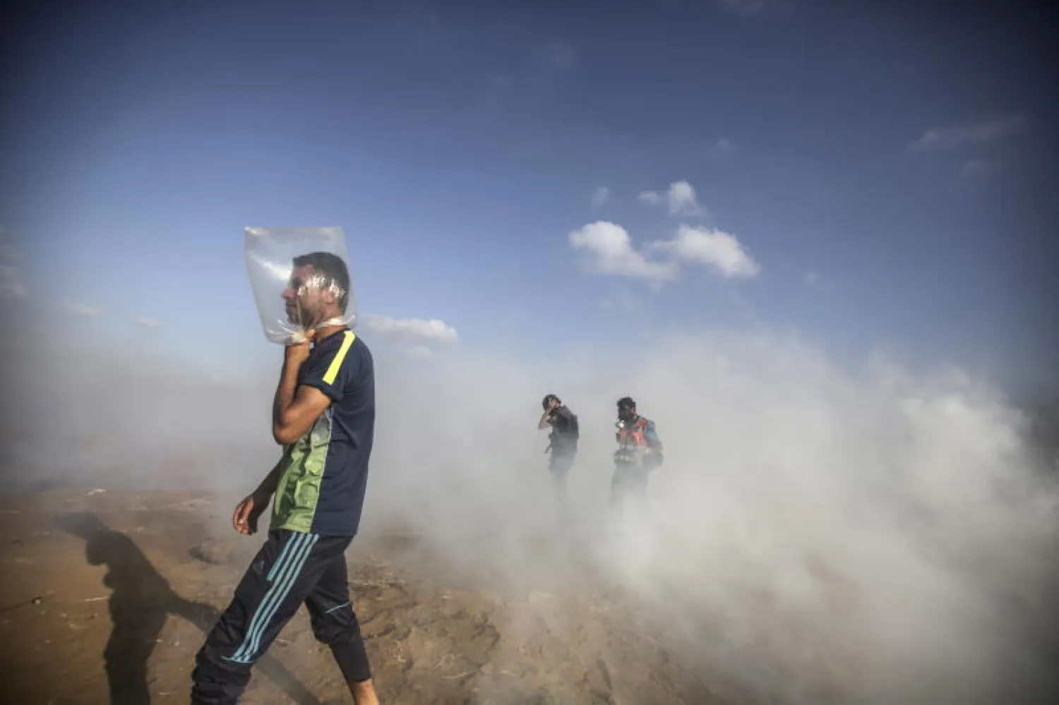 شاب فلسطيني يستخدم كيساً بلاستيكياً لحماية نفسه من الغاز المسيل للدموع خلال الاشتباكات (إ.ب.أ)