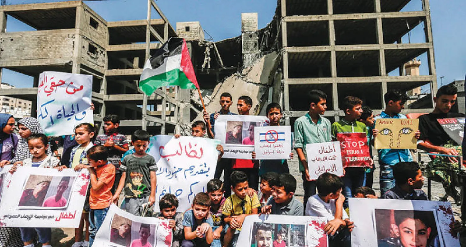 شبان وأطفال يتظاهرون رافعين العلم الفلسطيني أمام مبنى في غزة تعرض للقصف الإسرائيلي (أ.ف.ب)