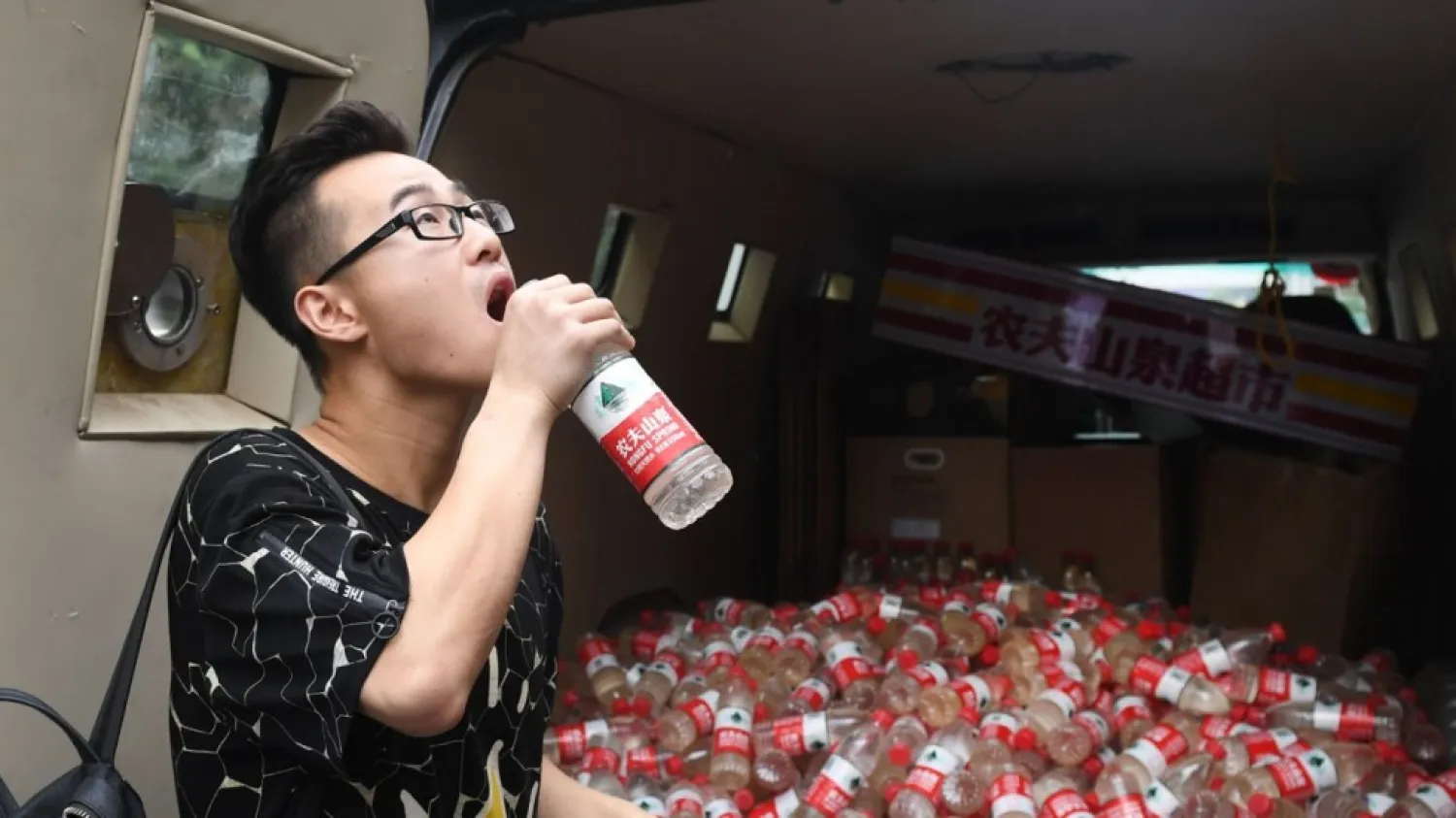 A pedestrian Yang Ziyi drinks a bottle of polluted groundwater from Xiaohaotu county, Yulin of Shaanxi province, at a roaming exhibition by Chinese performance artist "Nut Brother", in Beijing 798 art area, China July 12, 2018. | AFP