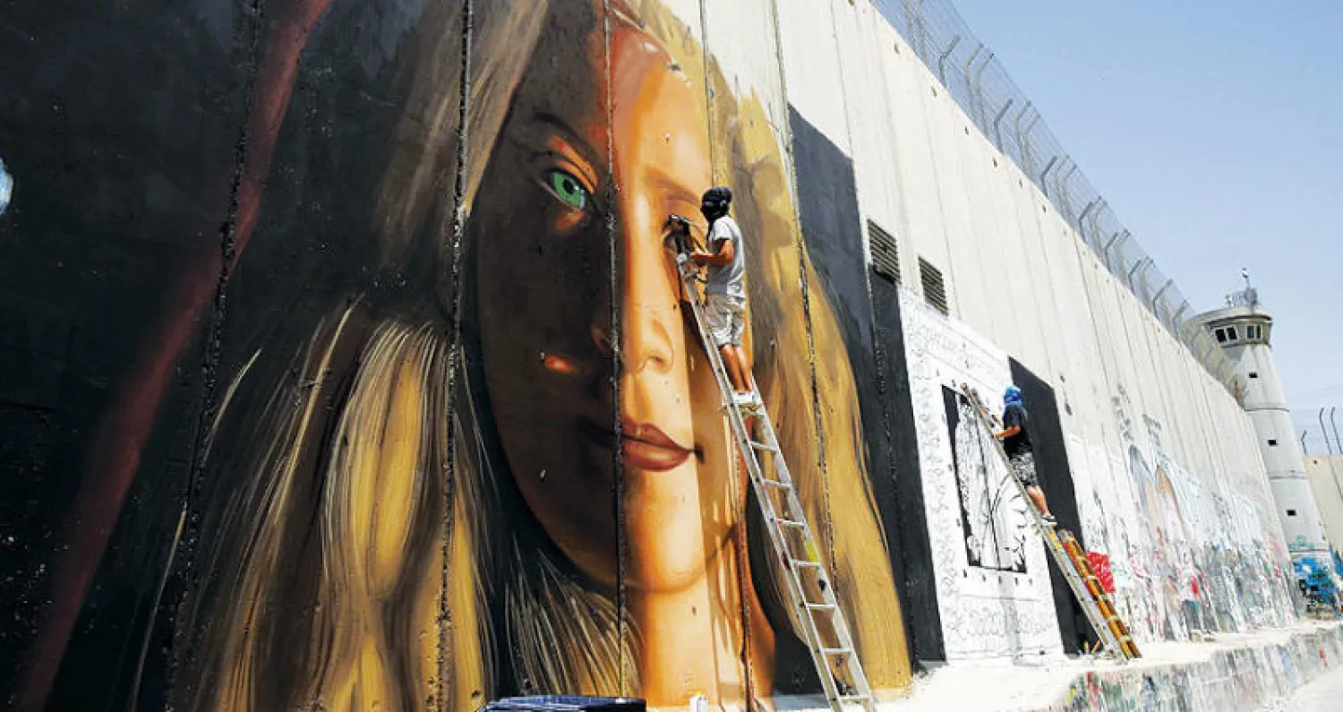 الفنان الإيطالي جوريت أغوش يضع اللمسات الأخيرة على لوحة رسمها لعهد التميمي على جدار الفصل العنصري قرب بيت لحم (أ.ف.ب)