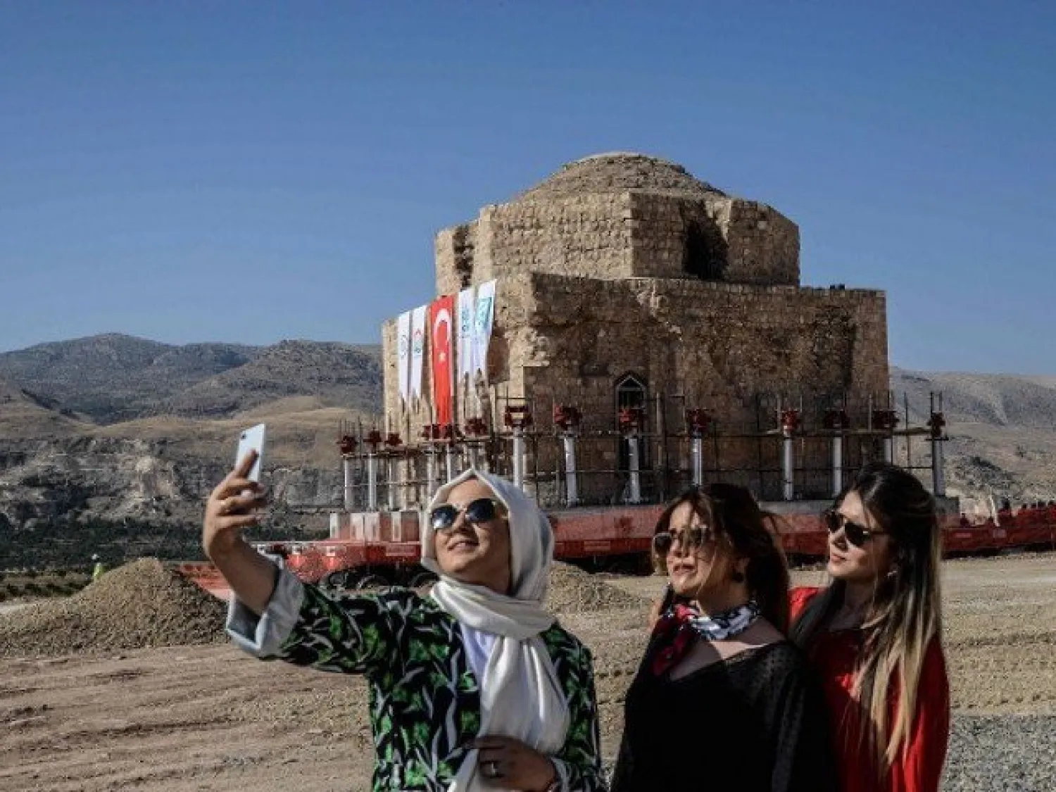 Women take a selfie picture with their mobile phone as the Artuklu Hamam is loaded onto a wheeled platform and moved down a specially constructed road, on August 6, 2018. AFP