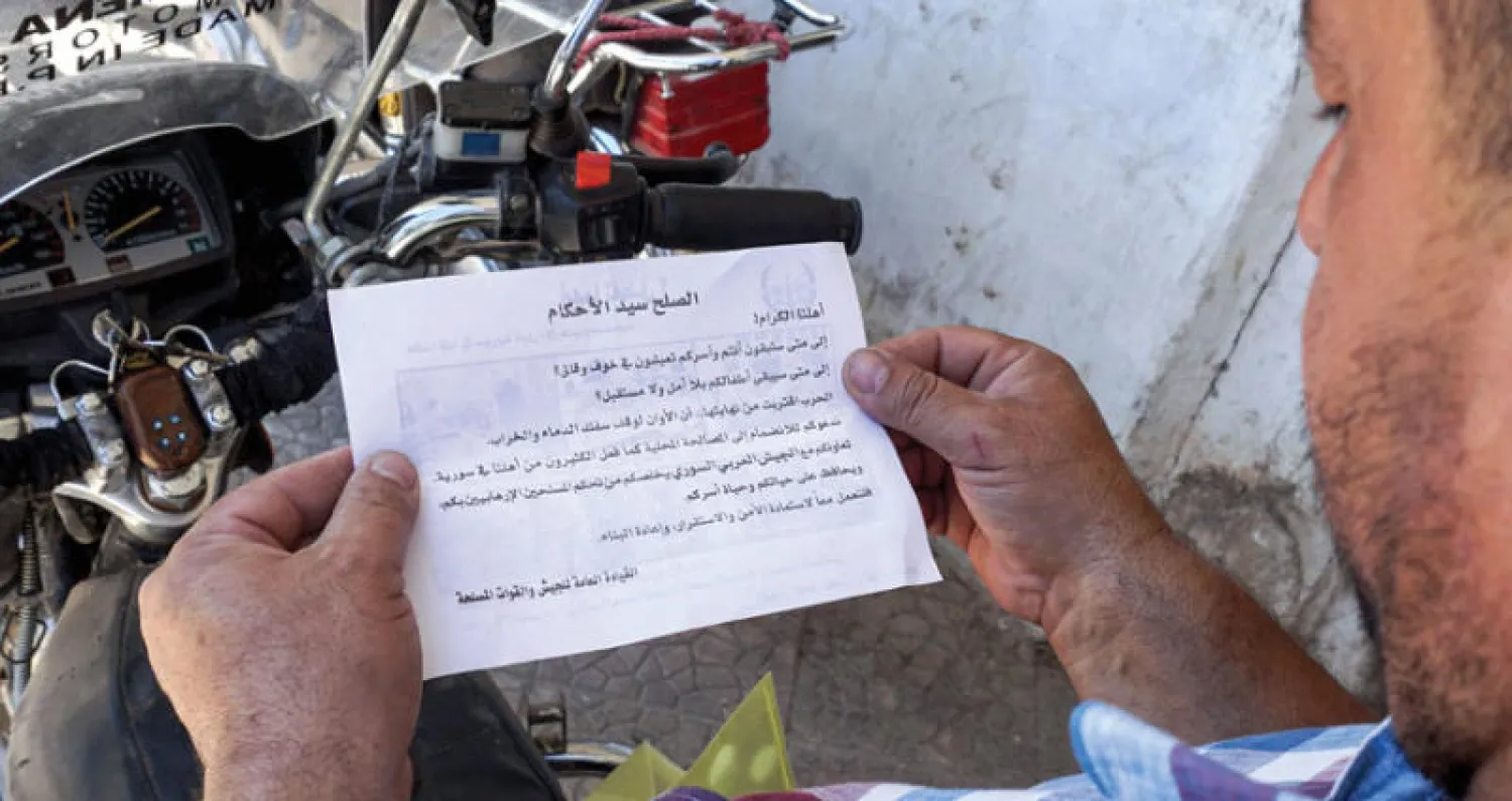 رجل من سكان بلدة سراقب بمحافظة إدلب يقرأ منشوراً رماه طيران النظام يدعو فيه للاستسلام (أ.ف.ب)