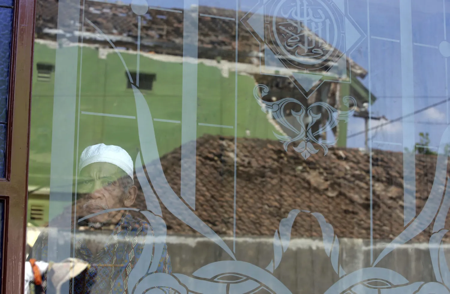 رجل ينظر من نافذة مسجد حيث انعكست صور المنازل المتضررة على الزجاج