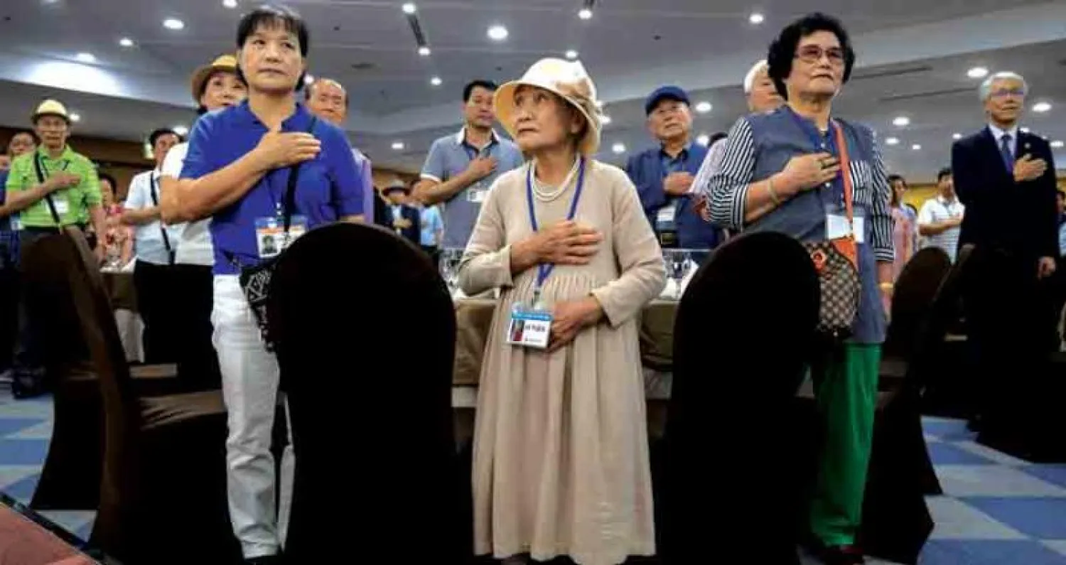 كوريون جنوبيون يقفون للنشيد الوطني قبل لقائهم أقارب انفصلوا عنهم قبل عقود في سوكشو أمس (أ.ف.ب)