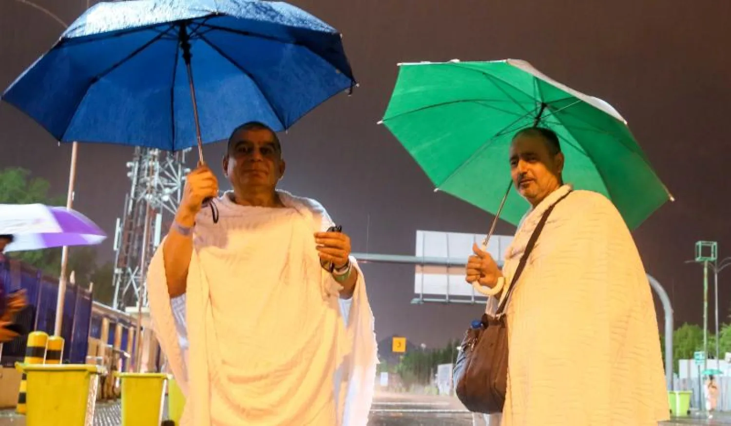 حاجان يحملان مظلتين أثناء هطول الأمطار على المشاعر المقدسة (تصوير: عبد الله الفالح)