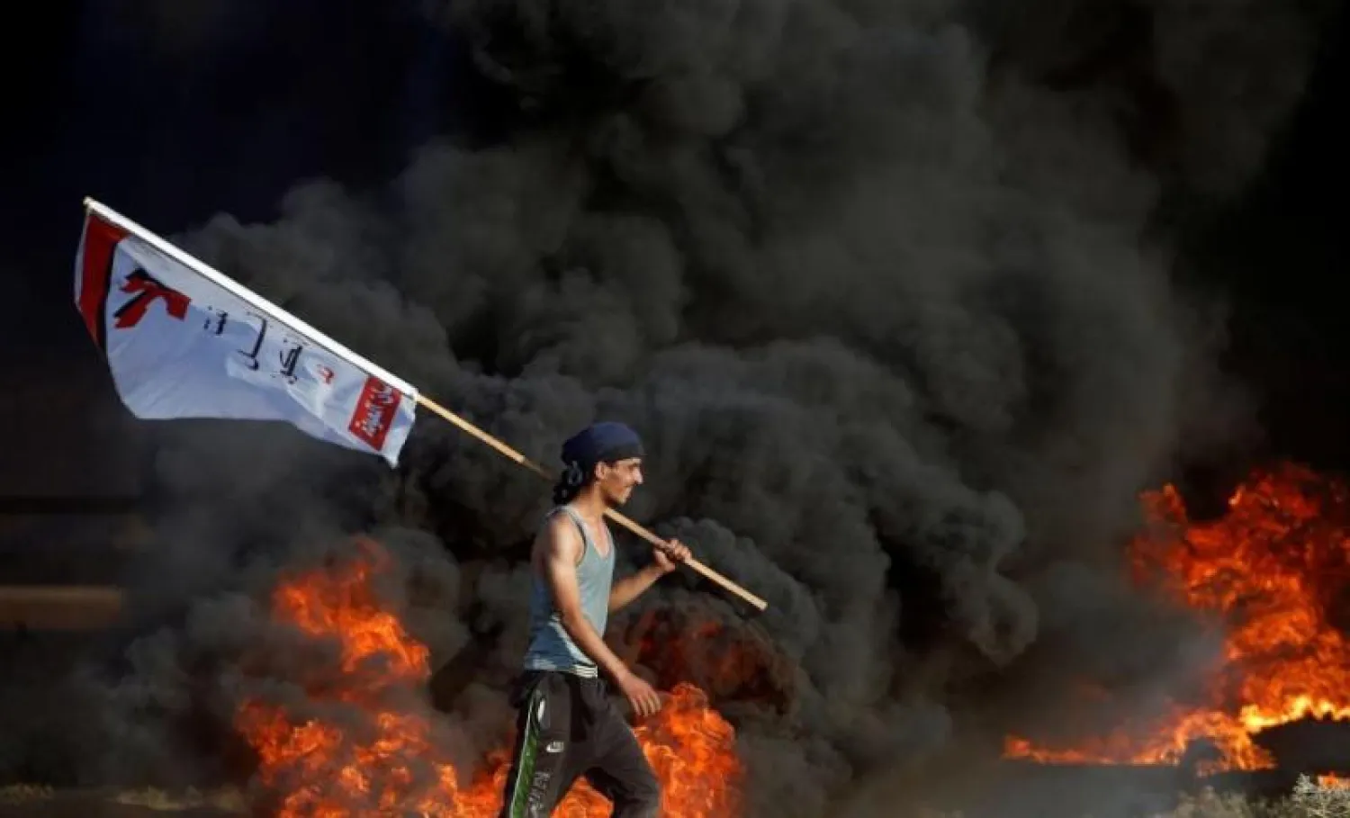 محتج فلسطيني يمر بجانب إطارات مشتعلة في احتجاجات على الحدود بين غزة وإسرائيل يوم الجمعة الماضي (رويترز)