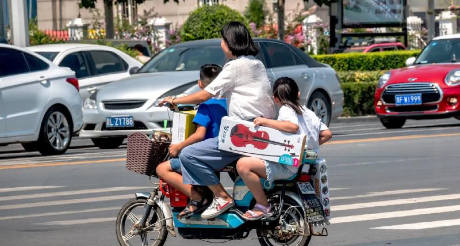 سيدة صينية مع طفليها على إحدى الدراجات البخارية (أ.ف.ب)