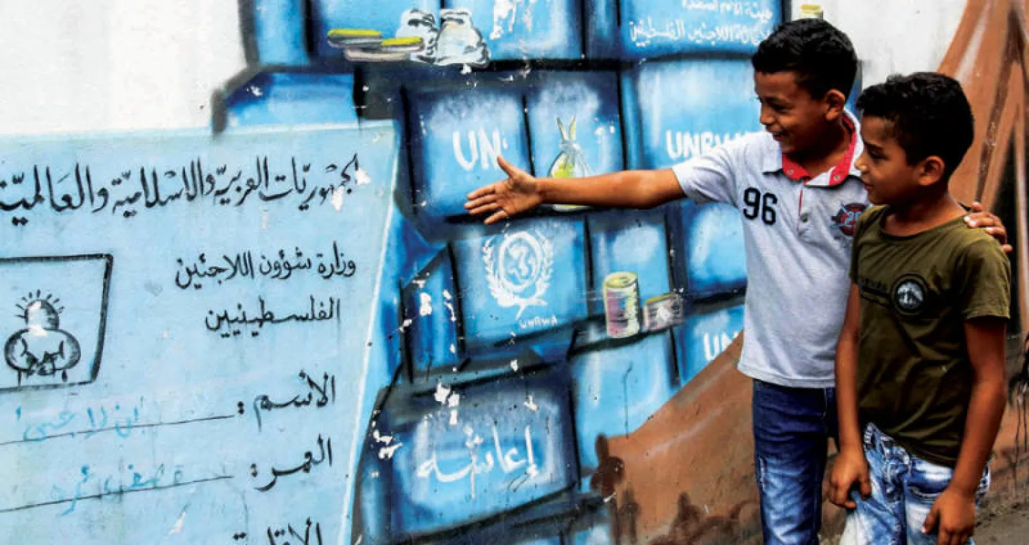 طفلان من مخيم «برج الشمالي» الفلسطيني قرب صور أمام لوح يقلد البطاقة الفلسطينية التي تحمل شعار الـ {أونروا} (إ ف ب)