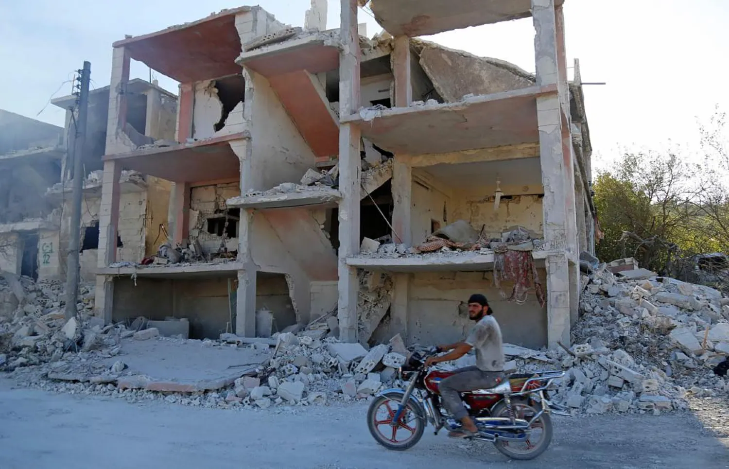 A Syrian man rides a motorcycle past a destroyed building in an area that was hit by a reported air strike in the district of Jisr al-Shughur, in the Idlib province, on Sept. 4, 2018. | AFP 