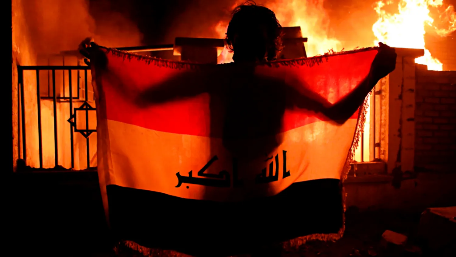 A man holds a national flag while protesters burn the municipal complex in Basra, Iraq. (AP)