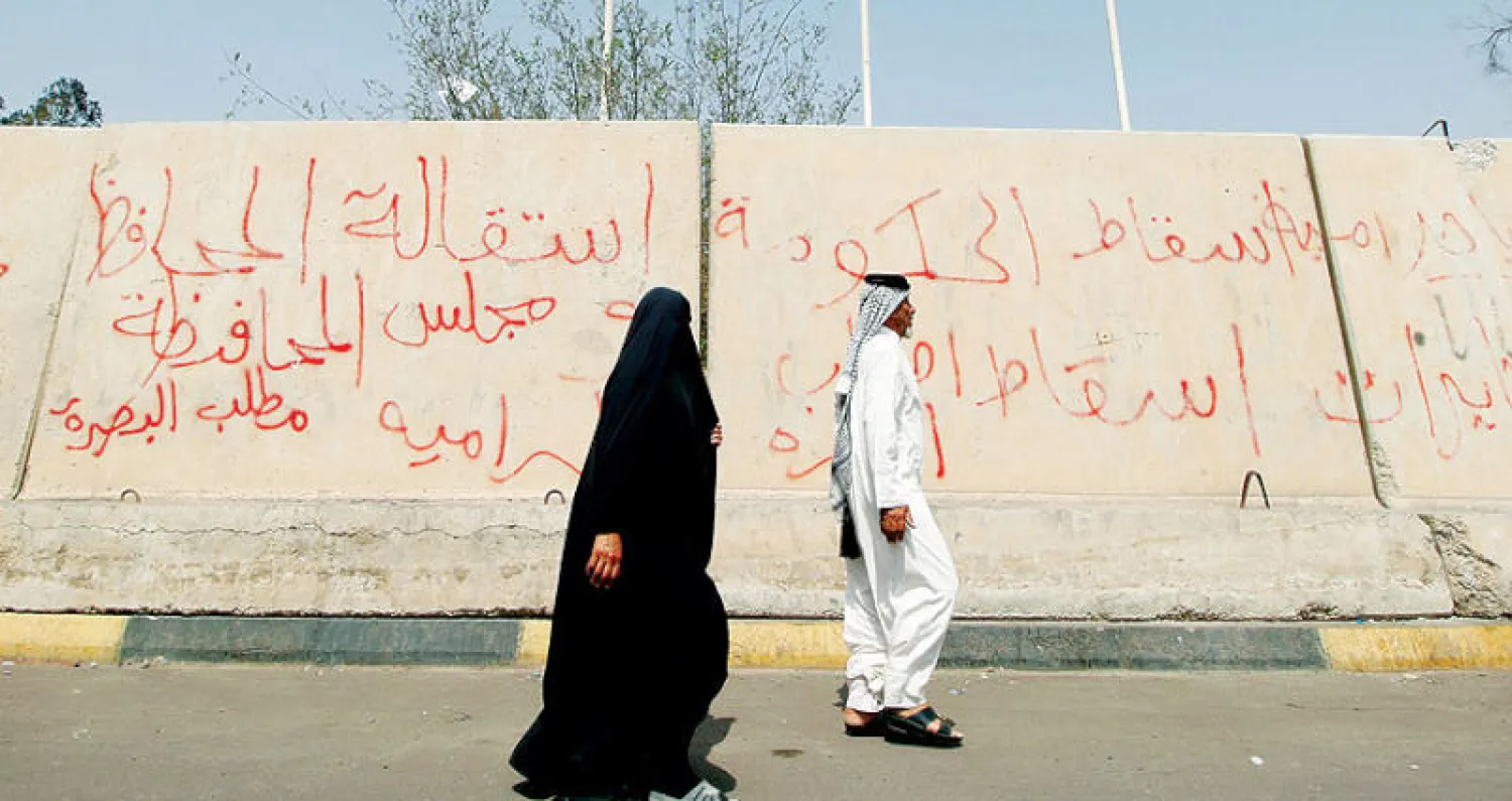 عراقيان يمران أمام جدار كتب عليه ناشطون شعارات ضد الحكومتين الاتحادية والمحلية في البصرة أمس (رويترز)