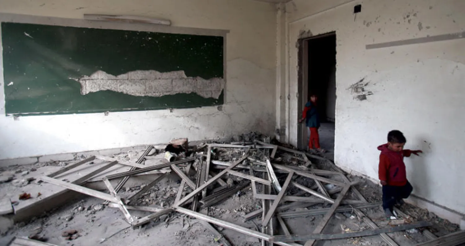 طفلان سوريان داخل أحد الصفوف في مدرسة تعرضت للدمار بشدة وتحولت ملجأ للنازحين في بلدة حمورية (غيتي)