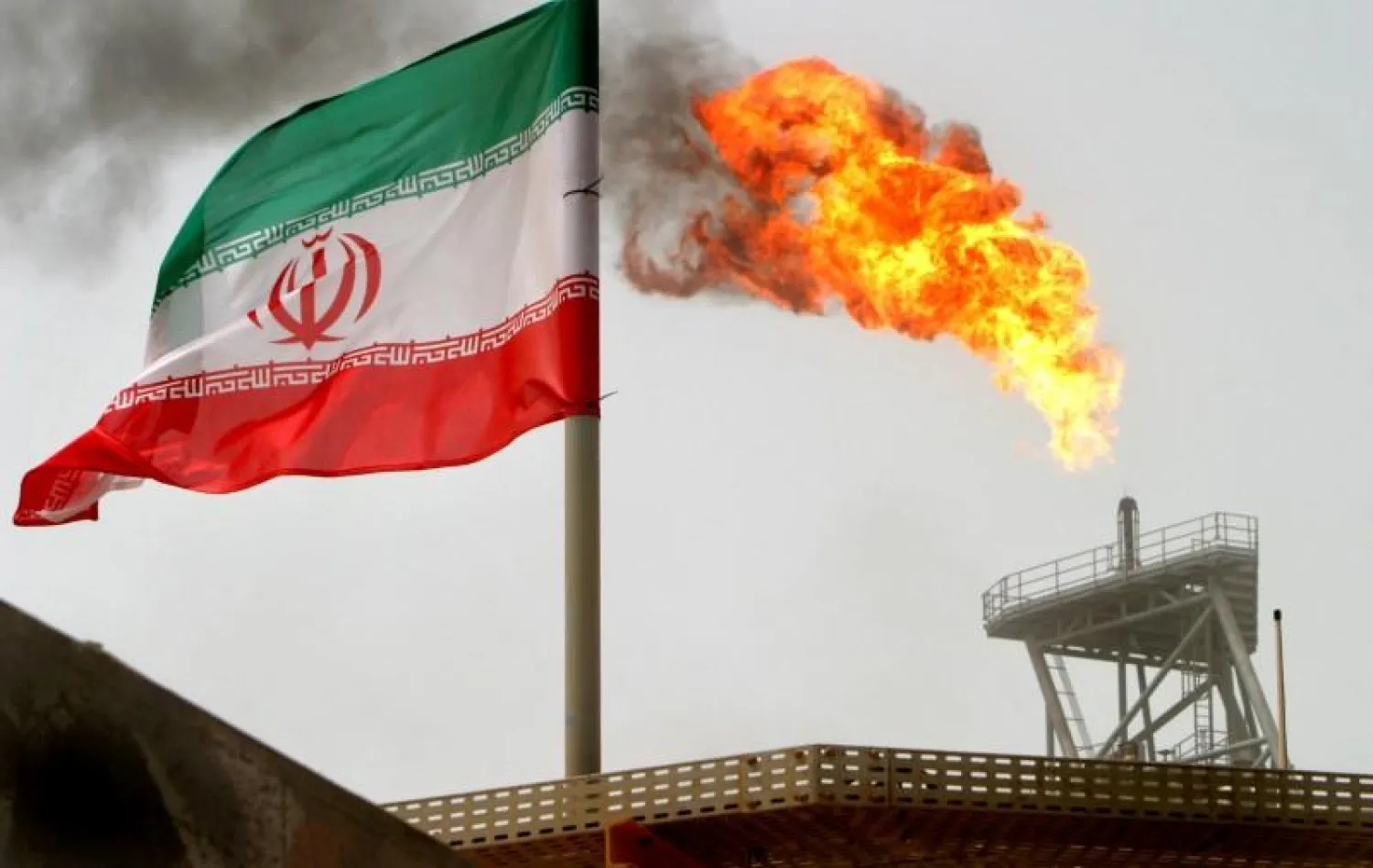 A gas flare on an oil production platform in the Soroush oil fields is seen alongside an Iranian flag in the Persian Gulf, Iran, July 25, 2005 | Reuters
