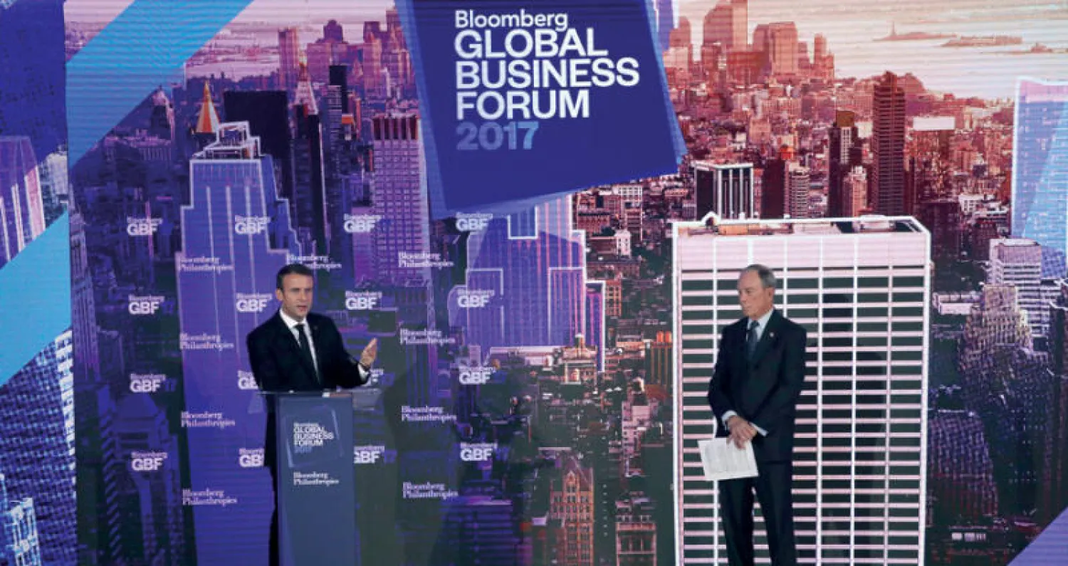 الرئيس الفرنسي إيمانويل ماكرون ومايكل بلومبرغ خلال منتدى العام الماضي (غيتي)